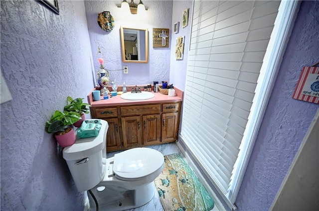 bathroom with toilet, vanity, and a textured wall