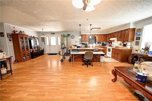 kitchen featuring light wood-type flooring, under cabinet range hood, white electric stove, stainless steel fridge, and light countertops