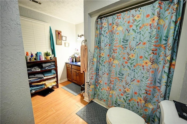 bathroom with toilet, curtained shower, a textured ceiling, wood finished floors, and a textured wall