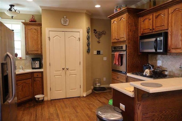 kitchen featuring ornamental molding, decorative backsplash, wood finished floors, light countertops, and appliances with stainless steel finishes