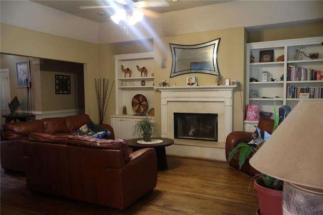 living room featuring a fireplace with raised hearth, a ceiling fan, and wood finished floors