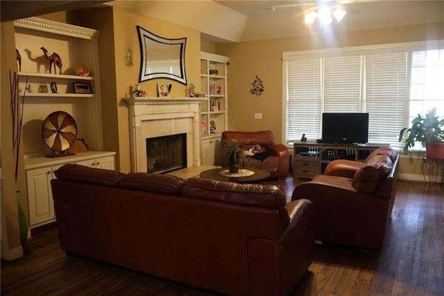 living area with dark wood-type flooring, built in features, ceiling fan, and a fireplace