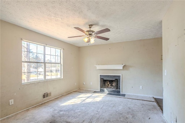 unfurnished living room with a textured ceiling, carpet floors, a fireplace with flush hearth, visible vents, and a ceiling fan