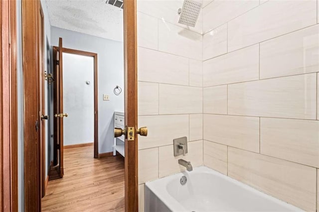 bathroom featuring a textured ceiling, wood-type flooring, and tiled shower / bath