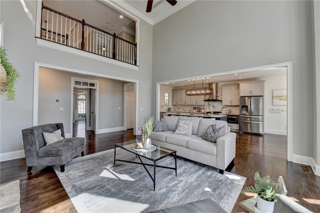 living area featuring dark wood-style flooring, baseboards, and ceiling fan with notable chandelier