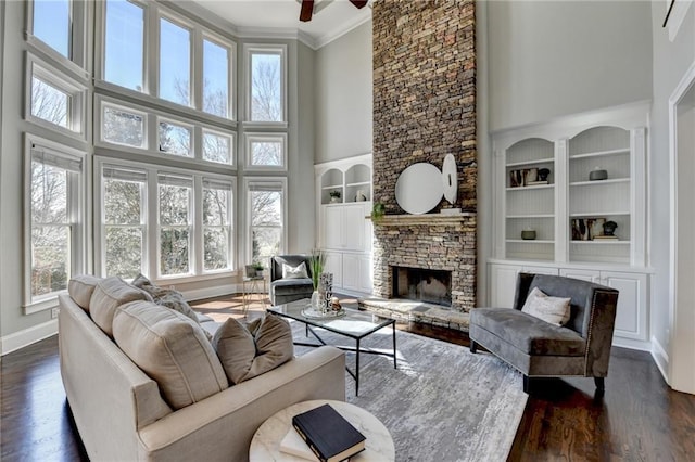 living area with built in shelves, a fireplace, dark wood finished floors, ornamental molding, and baseboards