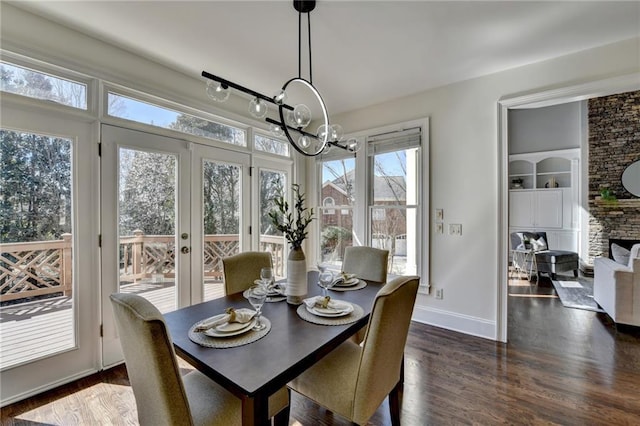 dining room featuring dark wood-style floors, built in features, an inviting chandelier, a stone fireplace, and baseboards