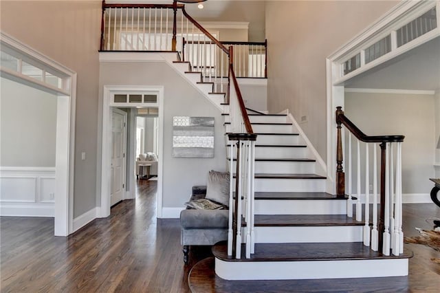 staircase featuring a high ceiling, baseboards, wood finished floors, and ornamental molding