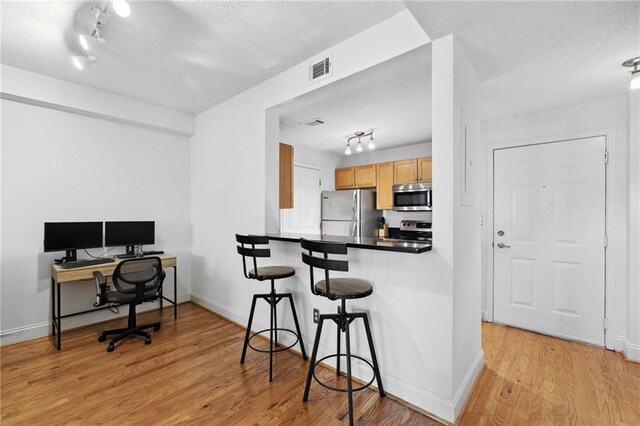 kitchen with a breakfast bar, a textured ceiling, rail lighting, light wood-style flooring, and stainless steel appliances