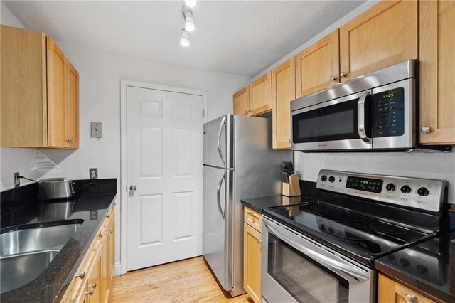 kitchen featuring appliances with stainless steel finishes, light wood-type flooring, a sink, dark stone countertops, and light brown cabinets