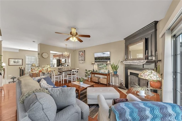 living area featuring a fireplace with flush hearth, ceiling fan with notable chandelier, and wood finished floors