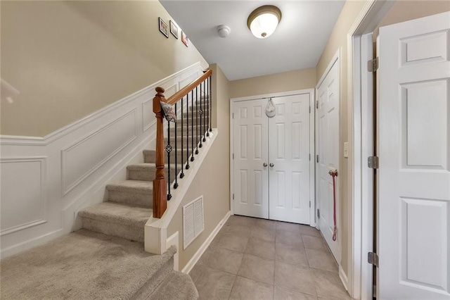 interior space featuring light tile patterned flooring, a decorative wall, a wainscoted wall, visible vents, and stairs