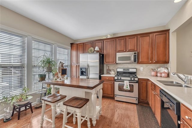 kitchen featuring brown cabinetry, decorative backsplash, stainless steel appliances, light wood-type flooring, and a sink