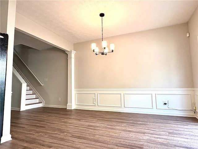 3884 Grovemont Pl, Duluth, GA 30096 - unfurnished dining area featuring a chandelier, dark wood-type flooring, stairway, a wainscoted wall, and ornate columns