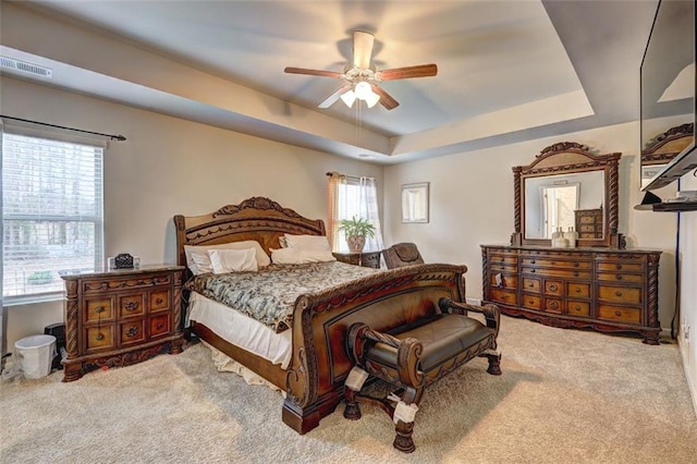 carpeted bedroom with a raised ceiling, multiple windows, and ceiling fan