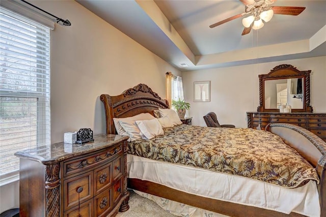 bedroom with a raised ceiling, multiple windows, ceiling fan, and light carpet