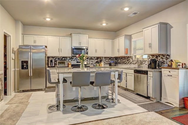 kitchen featuring a kitchen bar, appliances with stainless steel finishes, decorative backsplash, sink, and a kitchen island