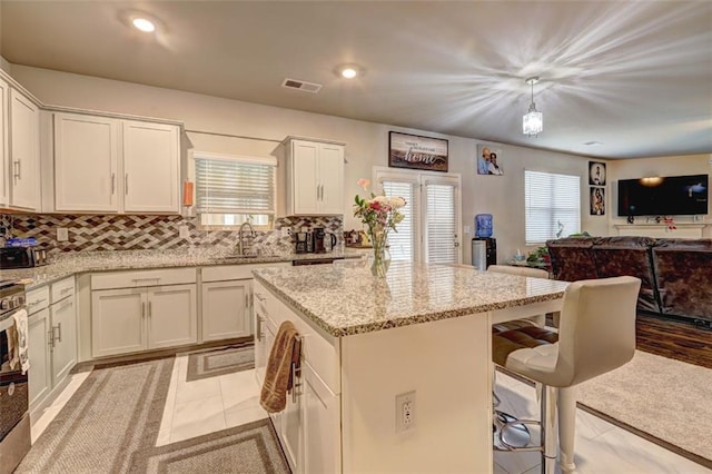 kitchen with light stone countertops, backsplash, sink, a center island, and hanging light fixtures