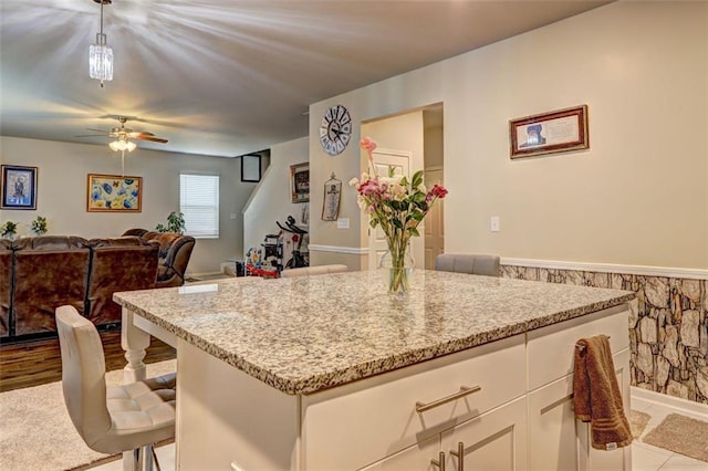 kitchen with white cabinets, decorative light fixtures, light stone counters, and a breakfast bar