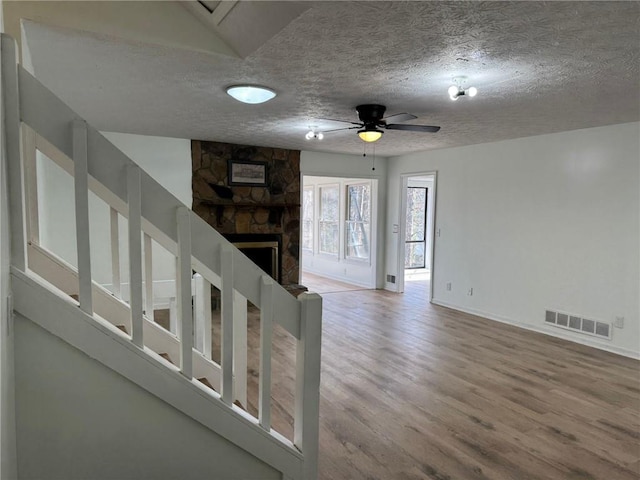 interior space featuring a textured ceiling, a fireplace, wood finished floors, visible vents, and a ceiling fan