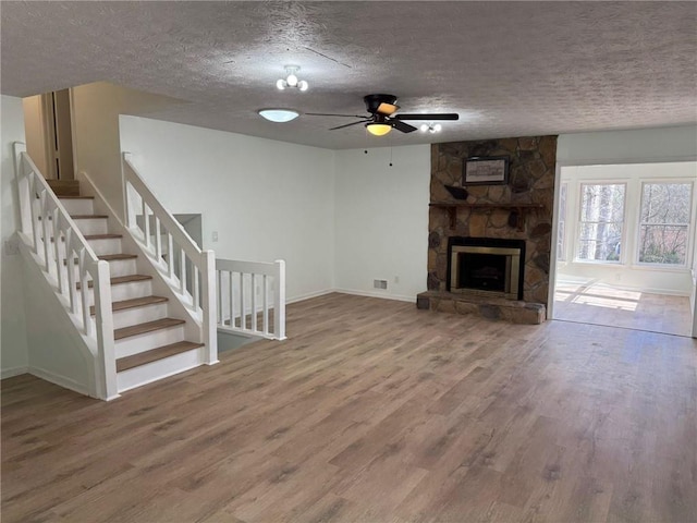 unfurnished living room featuring stairs, a stone fireplace, a textured ceiling, and wood finished floors