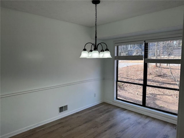 unfurnished dining area with dark wood-type flooring, visible vents, baseboards, and an inviting chandelier