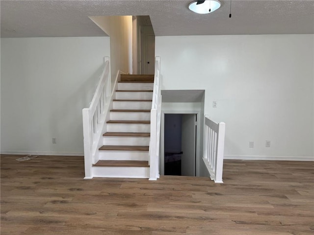 staircase featuring a textured ceiling, baseboards, and wood finished floors