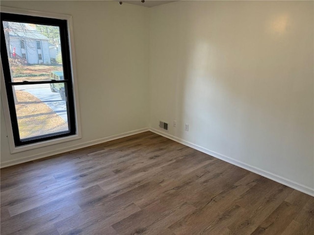 spare room featuring dark wood-style flooring, visible vents, and baseboards