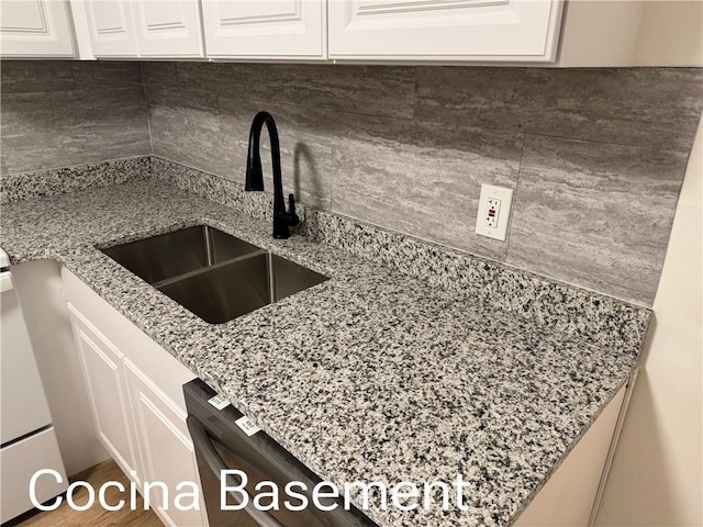 kitchen featuring tasteful backsplash, white cabinets, a sink, light stone countertops, and dishwasher