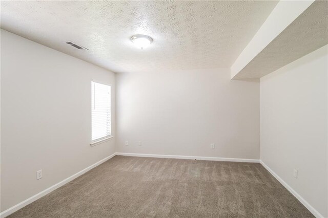 carpeted spare room featuring a textured ceiling, visible vents, and baseboards