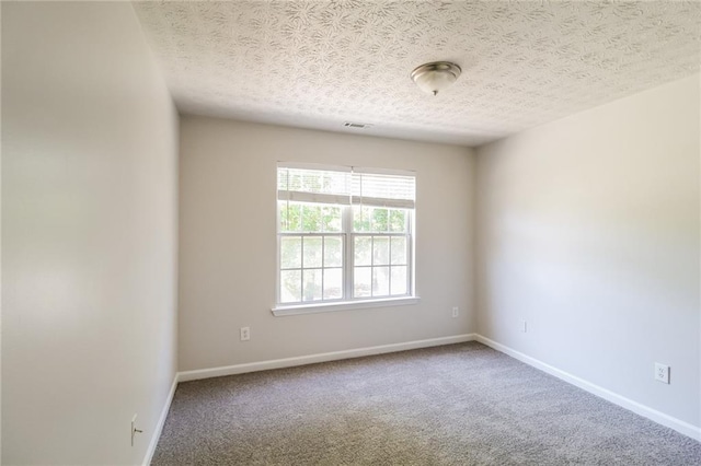 carpeted spare room featuring a textured ceiling, visible vents, and baseboards