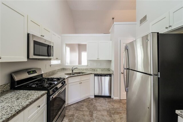 kitchen with lofted ceiling, sink, white cabinets, appliances with stainless steel finishes, and light stone counters