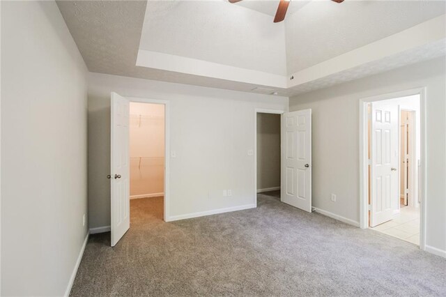 unfurnished bedroom featuring light carpet, a raised ceiling, ceiling fan, a spacious closet, and a closet