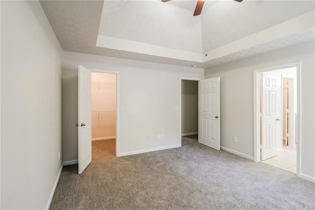 unfurnished bedroom featuring a walk in closet, ceiling fan, baseboards, a closet, and carpet flooring
