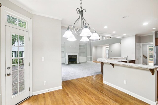 kitchen with light hardwood / wood-style flooring, decorative light fixtures, ornamental molding, a high end fireplace, and a notable chandelier