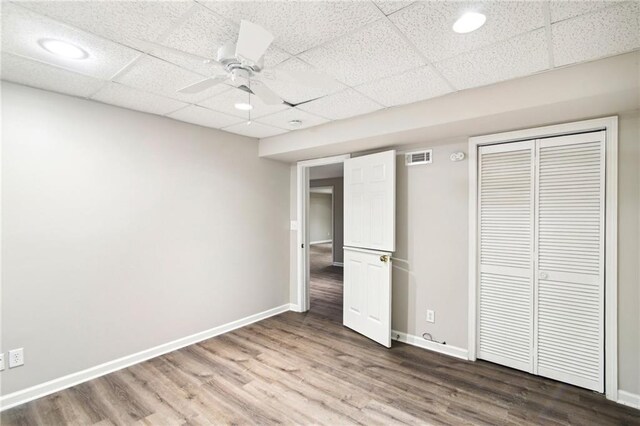 unfurnished bedroom featuring a drop ceiling, a closet, ceiling fan, and hardwood / wood-style floors