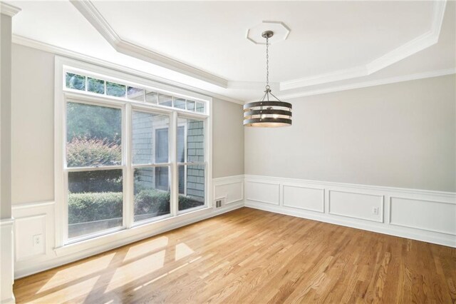 unfurnished dining area featuring hardwood / wood-style flooring, a raised ceiling, an inviting chandelier, and ornamental molding