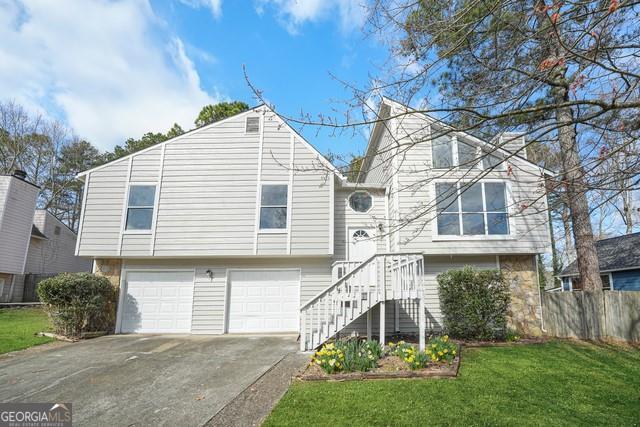split foyer home featuring fence, an attached garage, driveway, and a front lawn