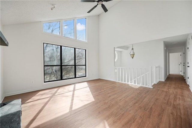 unfurnished living room with baseboards, high vaulted ceiling, ceiling fan, and wood finished floors