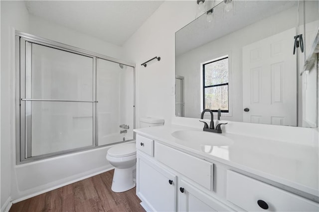 bathroom featuring toilet, enclosed tub / shower combo, wood finished floors, and vanity