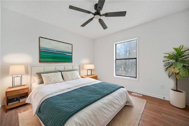 bedroom featuring ceiling fan, a textured ceiling, visible vents, wood finished floors, and baseboards