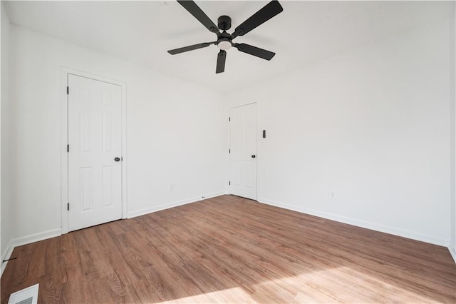 empty room with baseboards, ceiling fan, wood finished floors, and visible vents