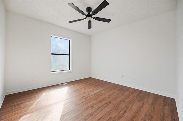 spare room with baseboards, a ceiling fan, wood finished floors, and visible vents