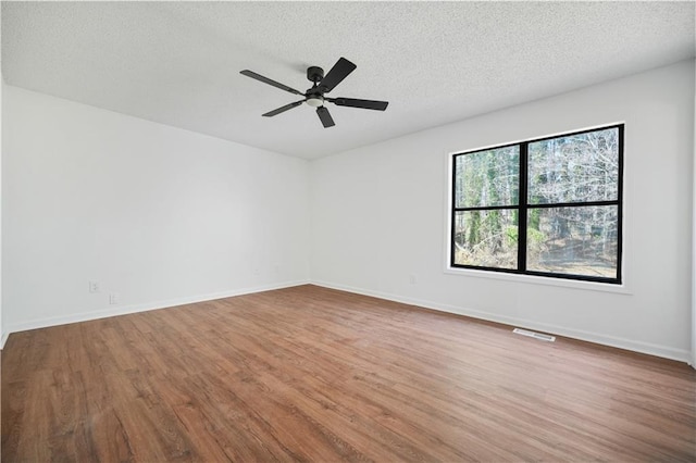 spare room with ceiling fan, a textured ceiling, baseboards, wood finished floors, and visible vents