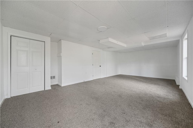 carpeted spare room featuring baseboards, visible vents, and a drop ceiling