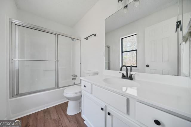 bathroom featuring toilet, wood finished floors, bath / shower combo with glass door, and vanity