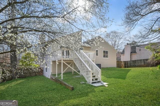 rear view of property featuring a lawn, stairs, a fenced backyard, and a wooden deck