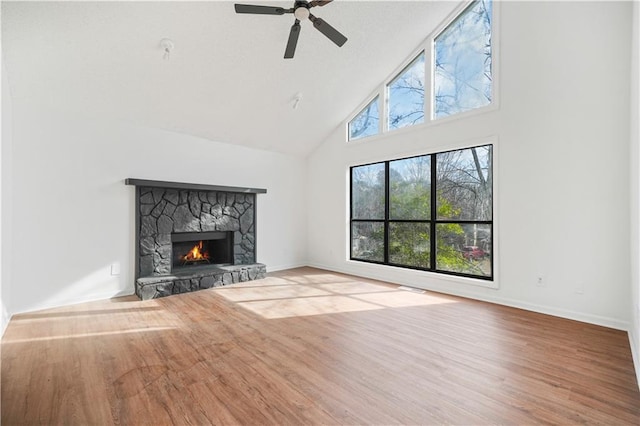 unfurnished living room with wood finished floors, a stone fireplace, baseboards, high vaulted ceiling, and a ceiling fan