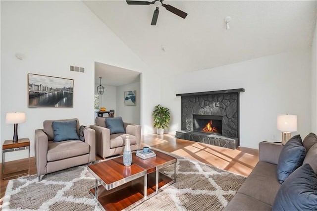 living area with a ceiling fan, visible vents, a fireplace, wood finished floors, and high vaulted ceiling