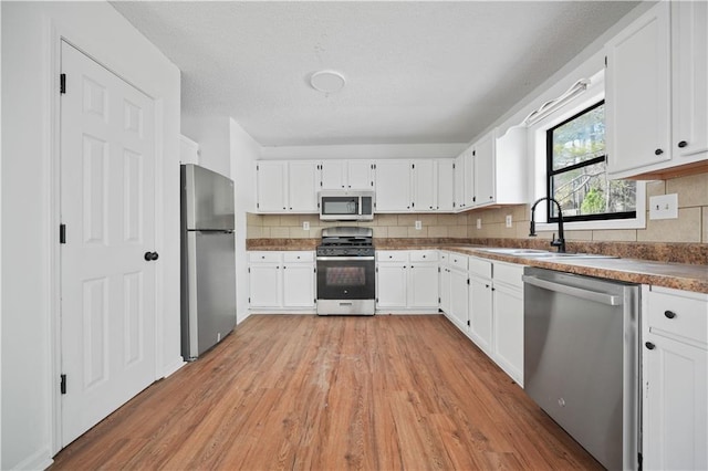 kitchen with decorative backsplash, a sink, white cabinets, light wood finished floors, and stainless steel appliances